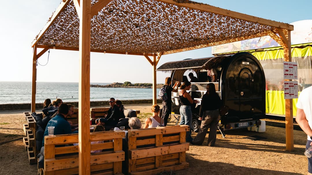 Rimorchio food truck in spiaggia, con i clienti seduti ai tavoli sotto il pergolato
